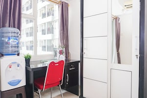 Habitación de hotel con escritorio, silla, dispensador de agua y vista del edificio.