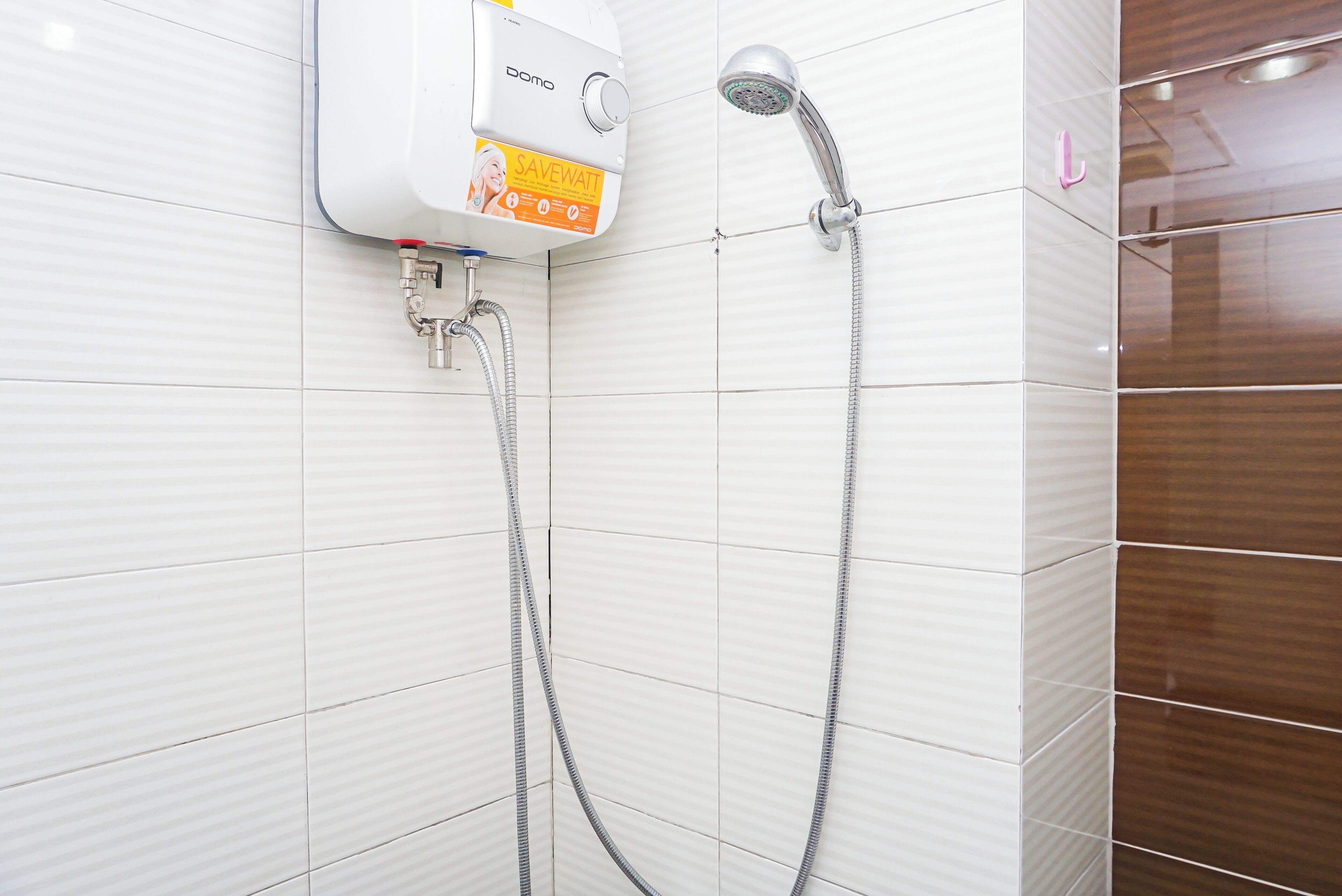 A bathroom with white tiled walls, a shower unit with a hose, and a visible water outlet.