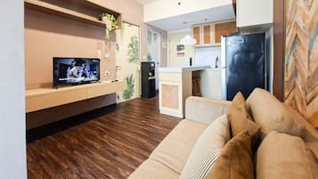 En moderne stue med sofa, fladskærms-tv, et køkkenområde med køleskab og trægulv.