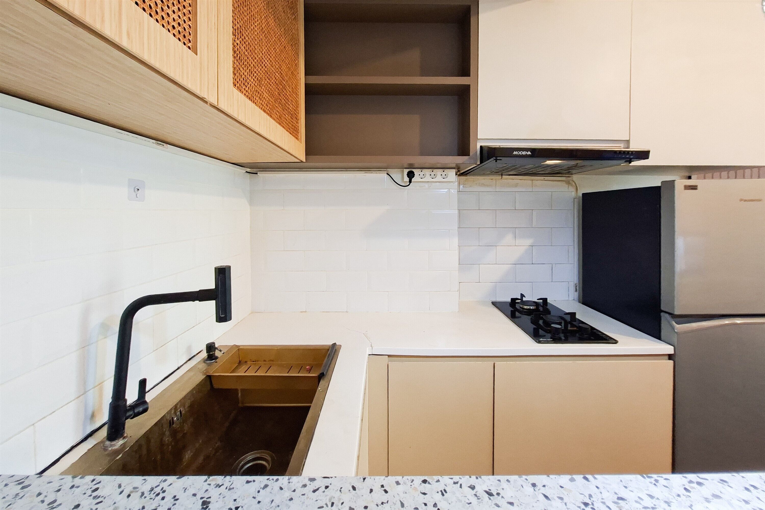 Une cuisine compacte avec des murs recouverts de carreaux blancs, une cuisinière à gaz encastrée, un réfrigérateur noir et des placards en bois.