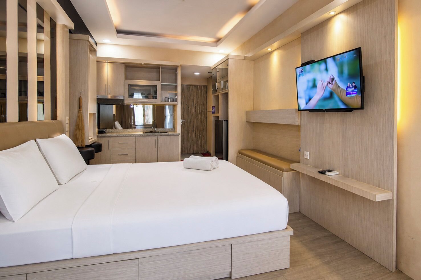 A hotel room with a large bed, a TV mounted on the wall, and a built-in kitchen area.
