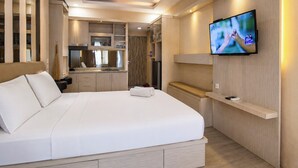 Ein Hotelzimmer mit einem großen Bett, einem an der Wand befestigten Fernseher und einer integrierten Küchenzeile.