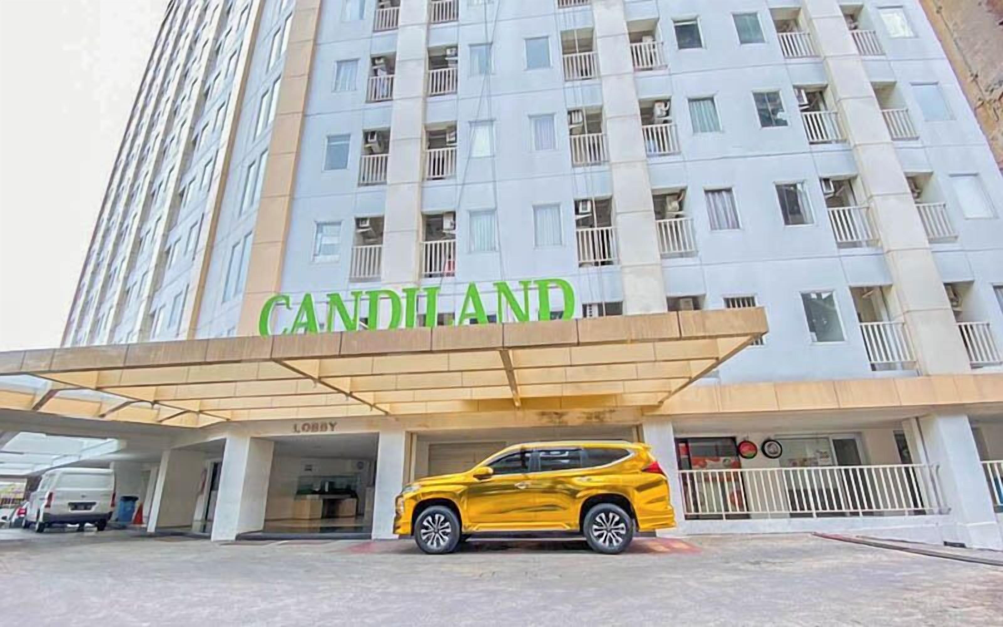 A hotel entrance with a yellow SUV parked in front, a covered lobby area, and a multi-story building with balconies.