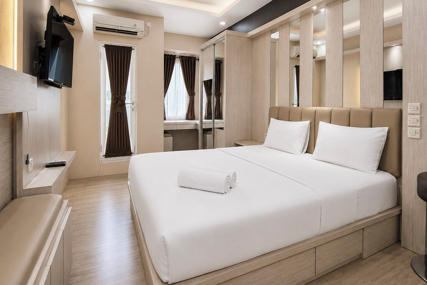 A hotel room with a large bed, a flat-screen TV mounted on the wall, and a window with curtains.