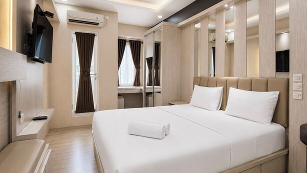 Ein Hotelzimmer mit einem großen Bett, einem an der Wand montierten Flachbildfernseher und einem Fenster mit Vorhängen.