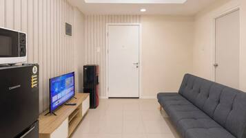 Una sala de estar moderna con un televisor de pantalla plana, un refrigerador, una computadora de escritorio y un sofá gris.