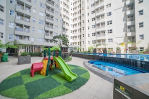 A residential building with a swimming pool, a children's play area, and a landscaped garden. - Bright And Homey 2Br At Apartment Parahyangan Residence (Bandung)