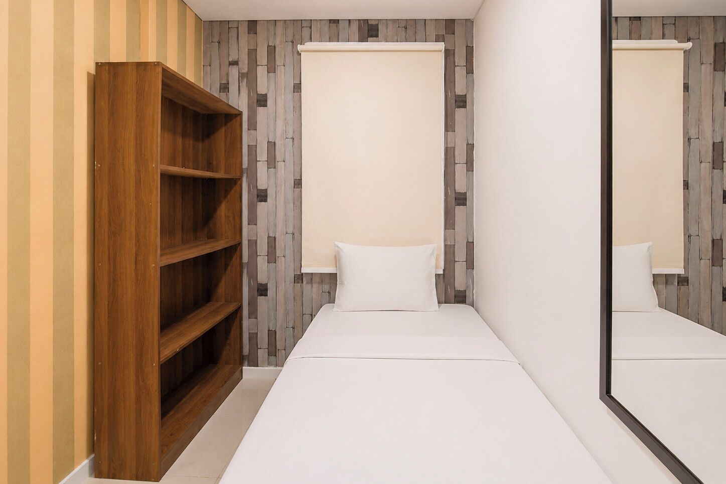 Una habitación pequeña con un armario de madera, una cama con ropa de cama blanca y un espejo que refleja el ambiente.