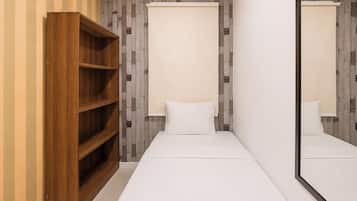 Una habitación pequeña con un armario de madera, una cama con ropa de cama blanca y un espejo que refleja el ambiente.