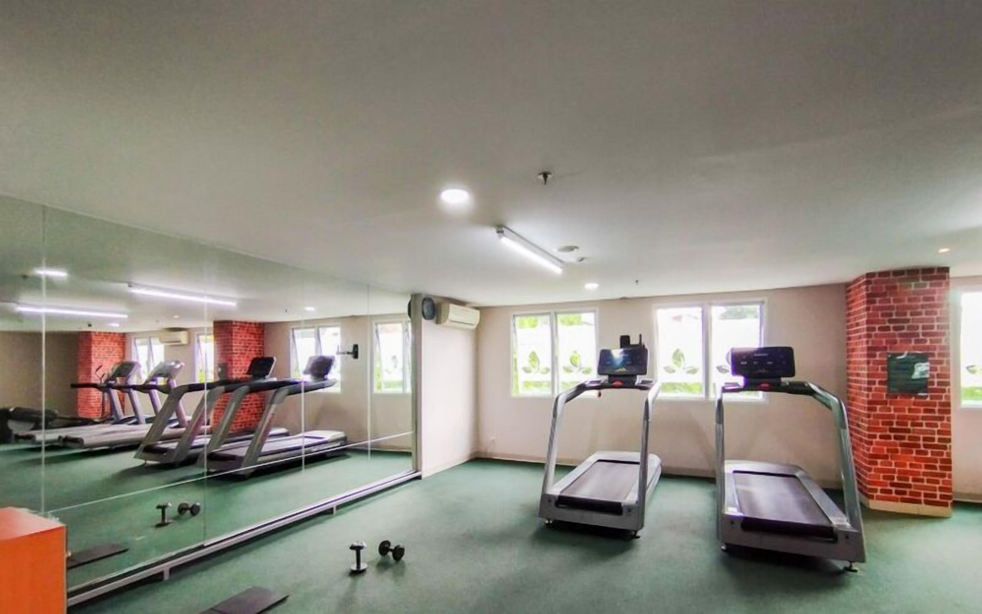 Un gimnasio con cintas de correr, un espejo y una alfombra verde.