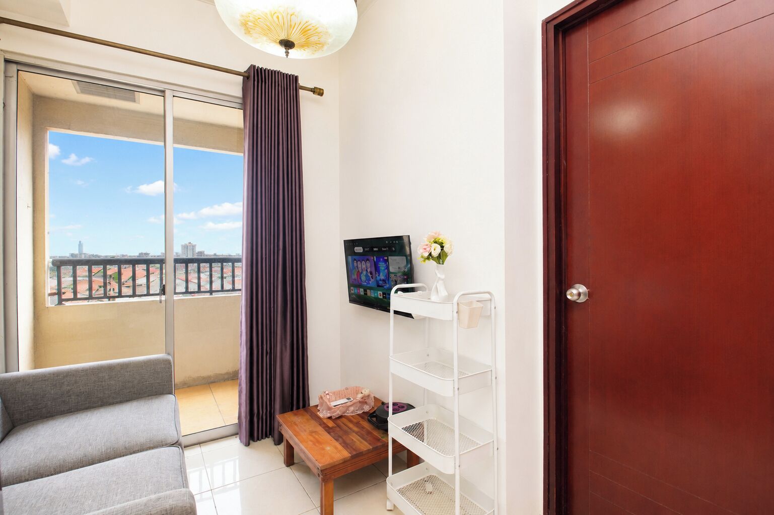 A room with a sofa, a small table, a TV mounted on the wall, and a door.