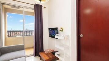 A room with a sofa, a small table, a TV mounted on the wall, and a door.