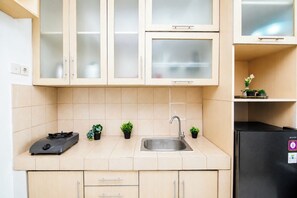A kitchen with a gas stove, sink, and a black refrigerator. There are cabinets with glass doors and a small shelf with plants. - Nice And Strategic 1Br At Apartment Marina Ancol (Jakarta)