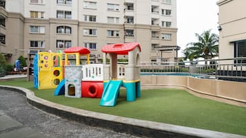 Un parque infantil con toboganes y estructuras para escalar, rodeado por una piscina y un edificio con balcones.