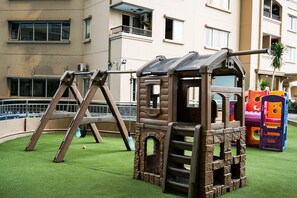 A children's play area with a wooden climbing structure, swings, and colorful play equipment. - Nice And Strategic 1Br At Apartment Marina Ancol (Jakarta)