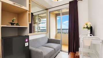 Un espacio habitable compacto con sofá, una mesita, refrigerador y vistas al exterior a través de una puerta corrediza de vidrio.