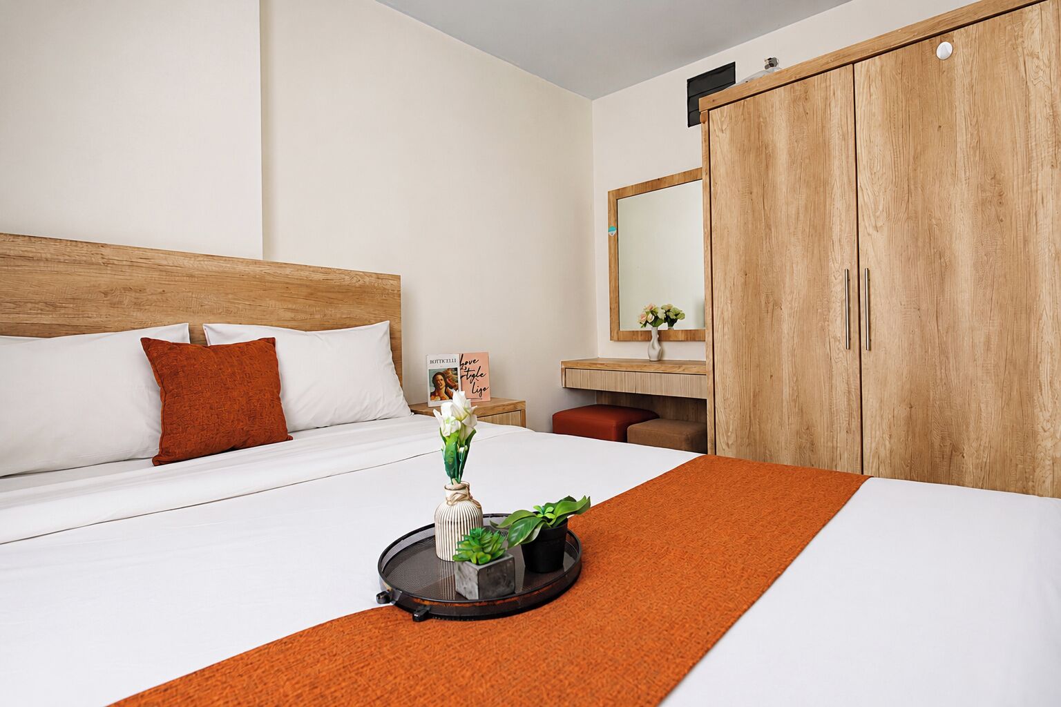Una camera d'albergo con un letto, un armadio in legno, un comodino con un vaso di fiori e uno specchio.