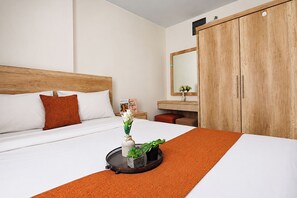 Una camera d'albergo con un letto, un armadio in legno, un comodino con un vaso di fiori e uno specchio.
