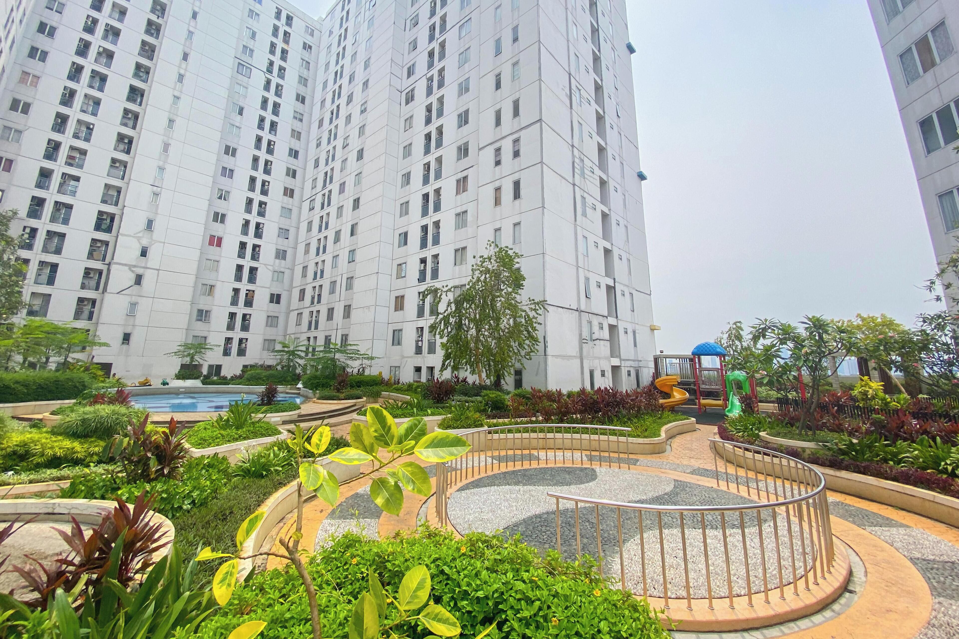 Un quartier résidentiel composé d’immeubles d’habitation à étages, d’un jardin aménagé avec un sentier circulaire et d’aires de jeux pour enfants.