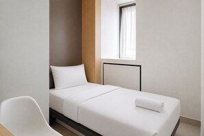 A single bed with a white mattress and pillow, a wooden headboard, a white chair, and a window with white curtains. - Good Minimalist Studio Room At Apartment Bandaraya - Tallasa City Makassar (Makassar (Ujung Pandang))