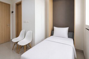 A hotel room with a bed, two white chairs, a wooden door, and a light switch on the wall. - Good Minimalist Studio Room At Apartment Bandaraya - Tallasa City Makassar (Makassar (Ujung Pandang))