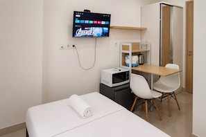 A hotel room with a bed, a desk, a microwave, a TV displaying 'Avengers', and a door. - Good Minimalist Studio Room At Apartment Bandaraya - Tallasa City Makassar (Makassar (Ujung Pandang))
