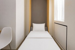 A narrow hotel room with a single bed, a chair, and a window. - Good Minimalist Studio Room At Apartment Bandaraya - Tallasa City Makassar (Makassar (Ujung Pandang))
