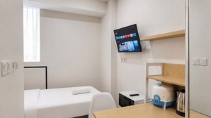 A hotel room with a bed, a desk, a television mounted on the wall, and a window. - Good Minimalist Studio Room At Apartment Bandaraya - Tallasa City Makassar (Makassar (Ujung Pandang))