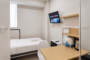 A hotel room with a bed, a desk, a television mounted on the wall, and a window. - Good Minimalist Studio Room At Apartment Bandaraya - Tallasa City Makassar (Makassar (Ujung Pandang))