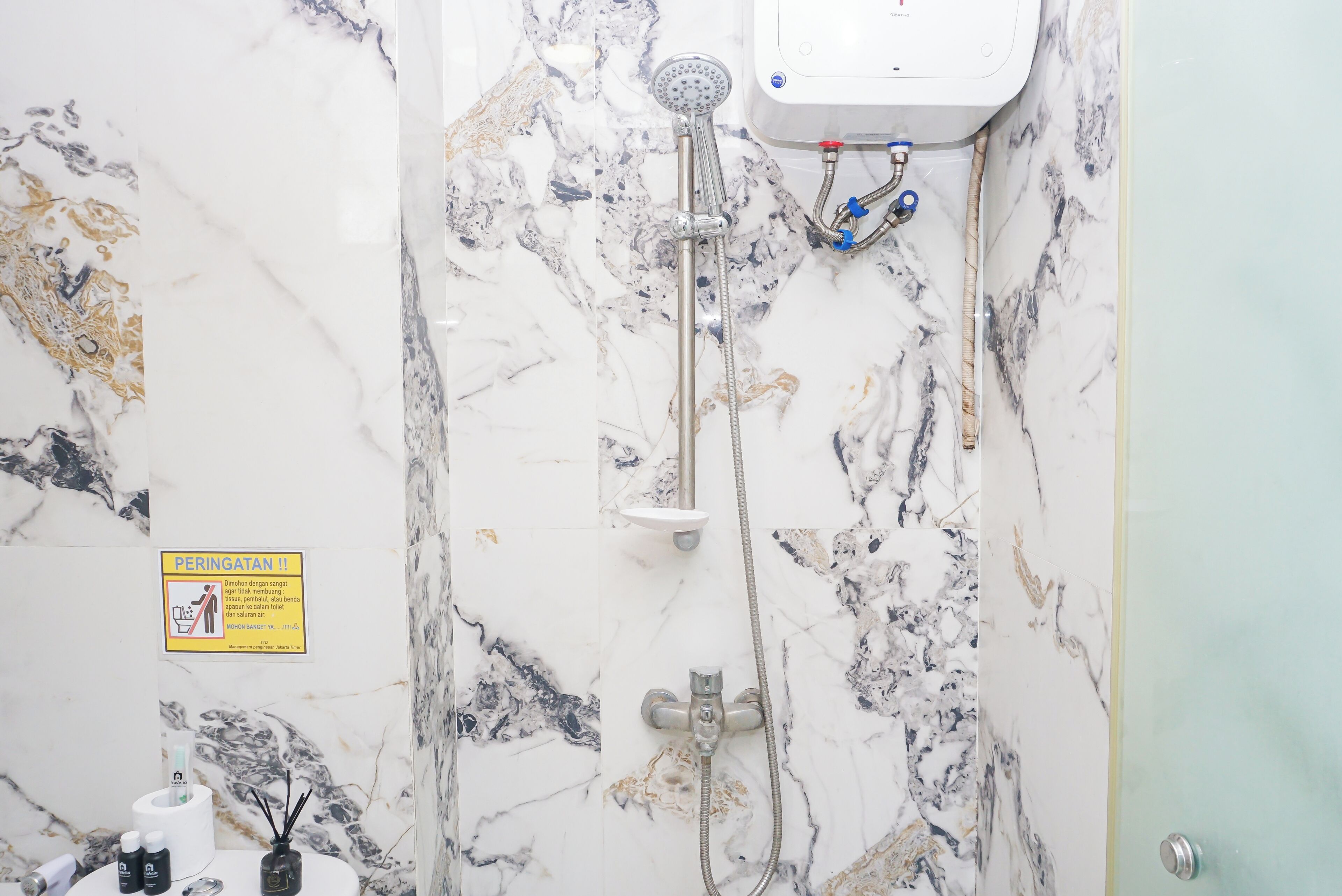 A bathroom with a shower, a toilet, and a sink. There is a sign on the wall and a bottle of hand soap on the counter.