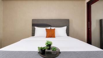 Una camera d'albergo con un letto, una testata, un comodino con vassoio e una pianta, e uno specchio.