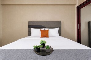 Una camera d'albergo con un letto, una testata, un comodino con vassoio e una pianta, e uno specchio.