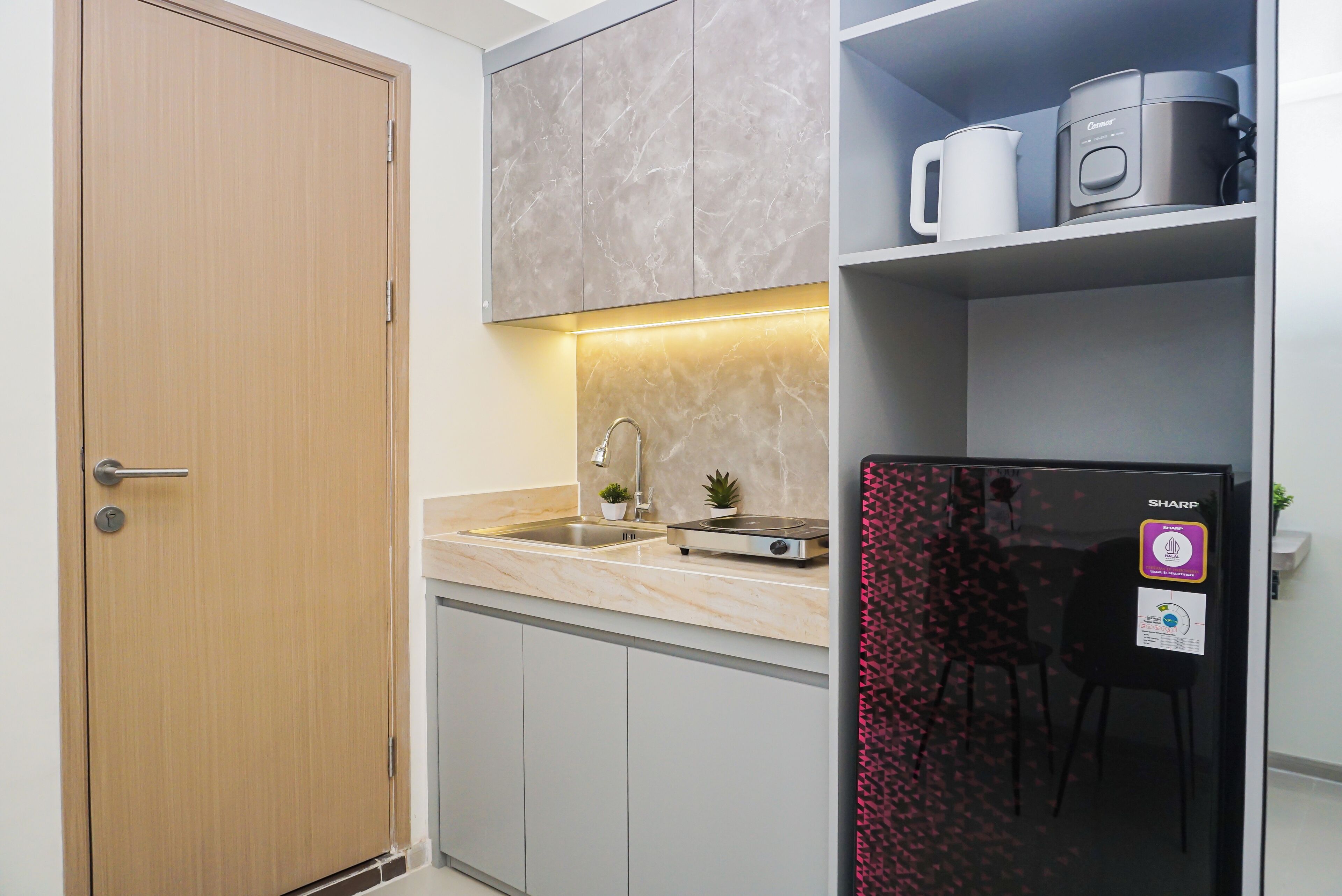 Cocina compacta con puerta de madera, encimera de mármol, horno integrado y refrigerador con etiqueta halal.