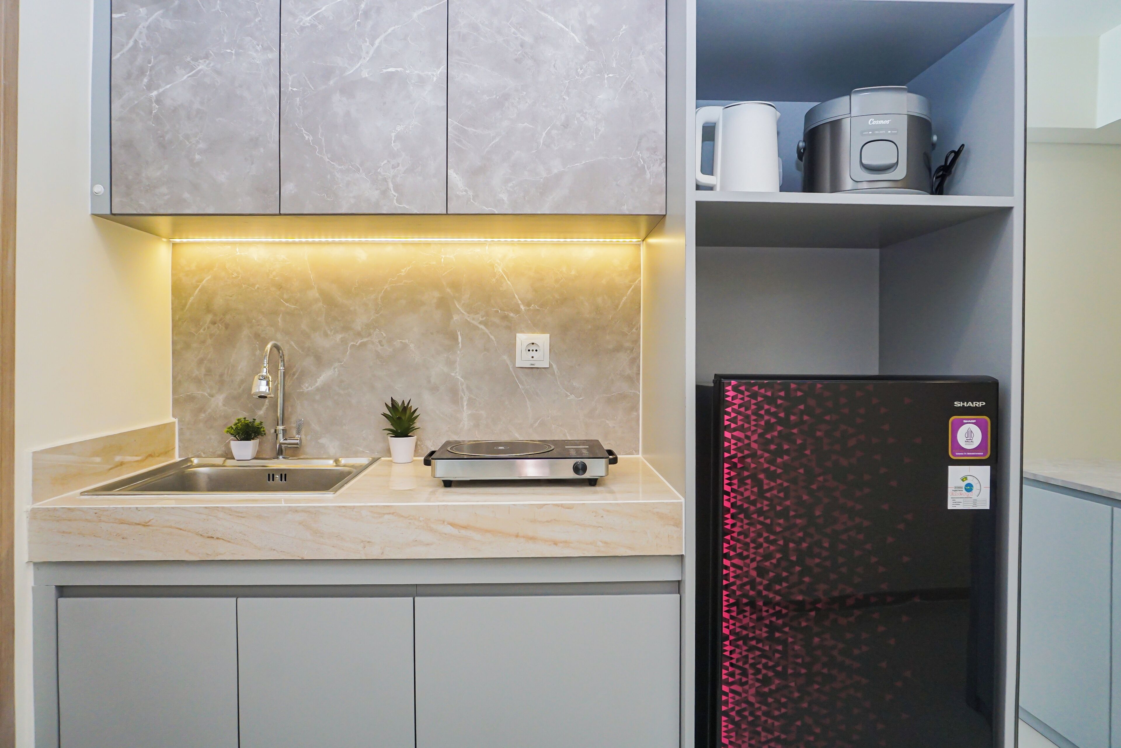 Una cocina con encimera de mármol, un fregadero, una pequeña planta en maceta, un tostador y un refrigerador con un estampado geométrico rojo.