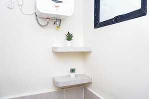 A bathroom with a white wall, a white heater, and two shelves with potted plants. - Comfortable Smart Studio Room At Apartment Meikarta District 2 (Cikarang)