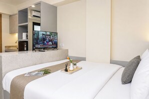 A hotel room with a bed, a TV on a stand, a small table with a tray, and a potted plant. - Comfortable Smart Studio Room At Apartment Meikarta District 2 (Cikarang)