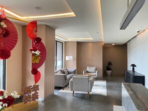 A modern hotel lobby with a reception desk, sofas, and a decorative wall with fans and flowers. - Comfortable Smart Studio Room At Apartment Meikarta District 2 (Cikarang)