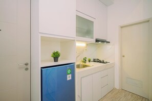 A compact kitchen with white cabinets, a blue refrigerator, a gas stove, and a small potted plant. - Warm Minimalist 2Br At Apartment Tokyo Riverside Pik 2 (Jakarta)