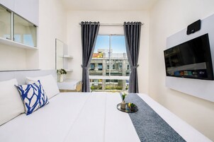 A hotel room with a bed, a TV, a window with curtains, and a view of buildings outside.