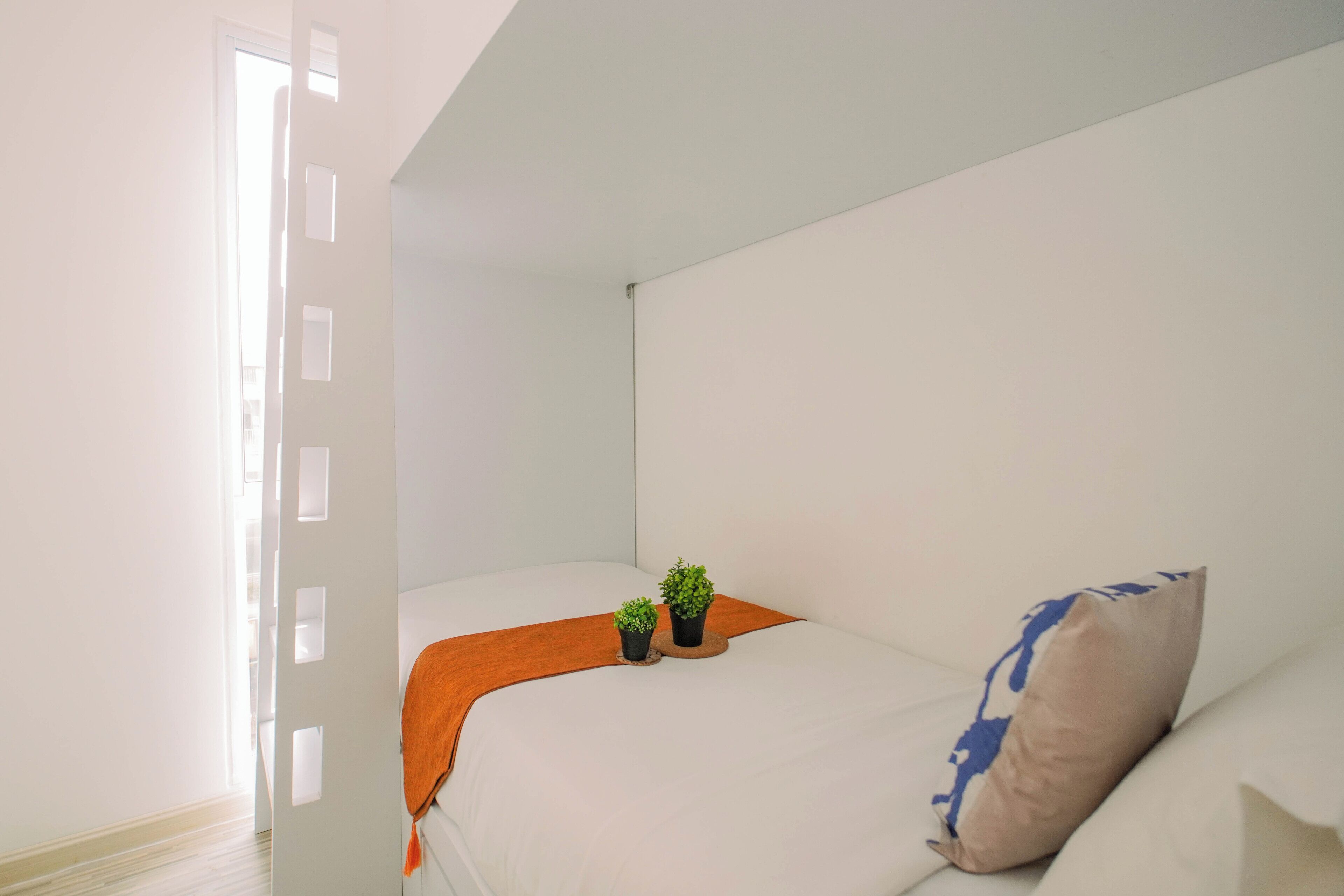 A minimalist bedroom with a bed, a small potted plant, and a throw blanket.