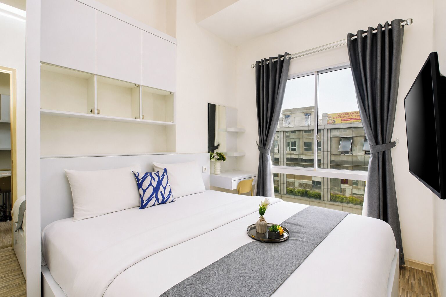A hotel room with a bed, a desk, a TV, and a window with curtains.