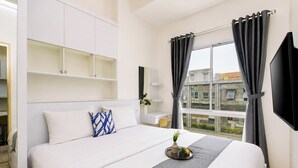 A hotel room with a bed, a desk, a TV, and a window with curtains. - Warm Minimalist 2Br At Apartment Tokyo Riverside Pik 2 (Jakarta)