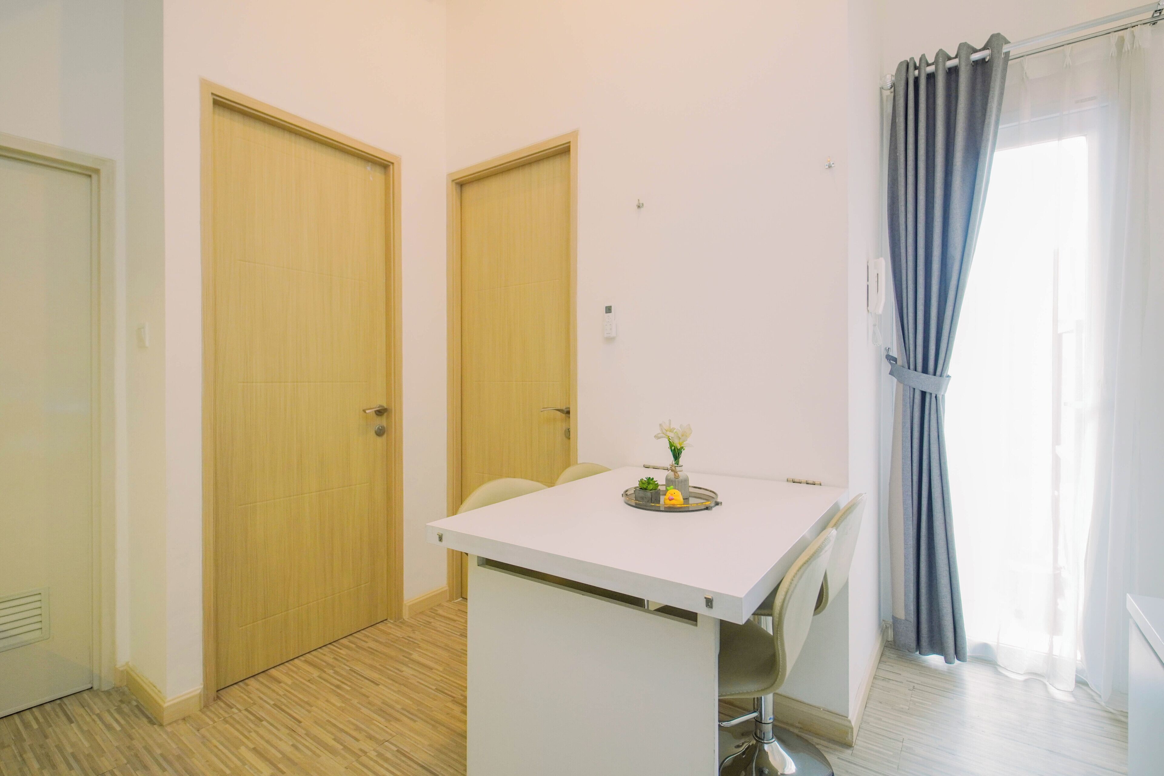A small, clean room with a white desk, two doors, a window with curtains, and a radiator.