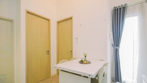 A small, clean room with a white desk, two doors, a window with curtains, and a radiator. - Warm Minimalist 2Br At Apartment Tokyo Riverside Pik 2 (Jakarta)