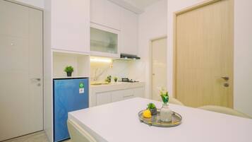 A compact kitchen with white cabinets, a blue refrigerator, and a dining area with a tray of food.