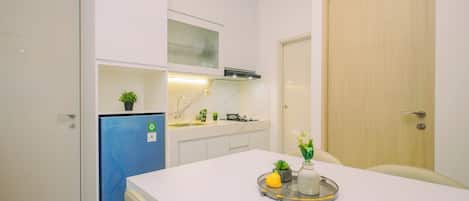 A compact kitchen with white cabinets, a blue refrigerator, and a dining area with a tray of food.