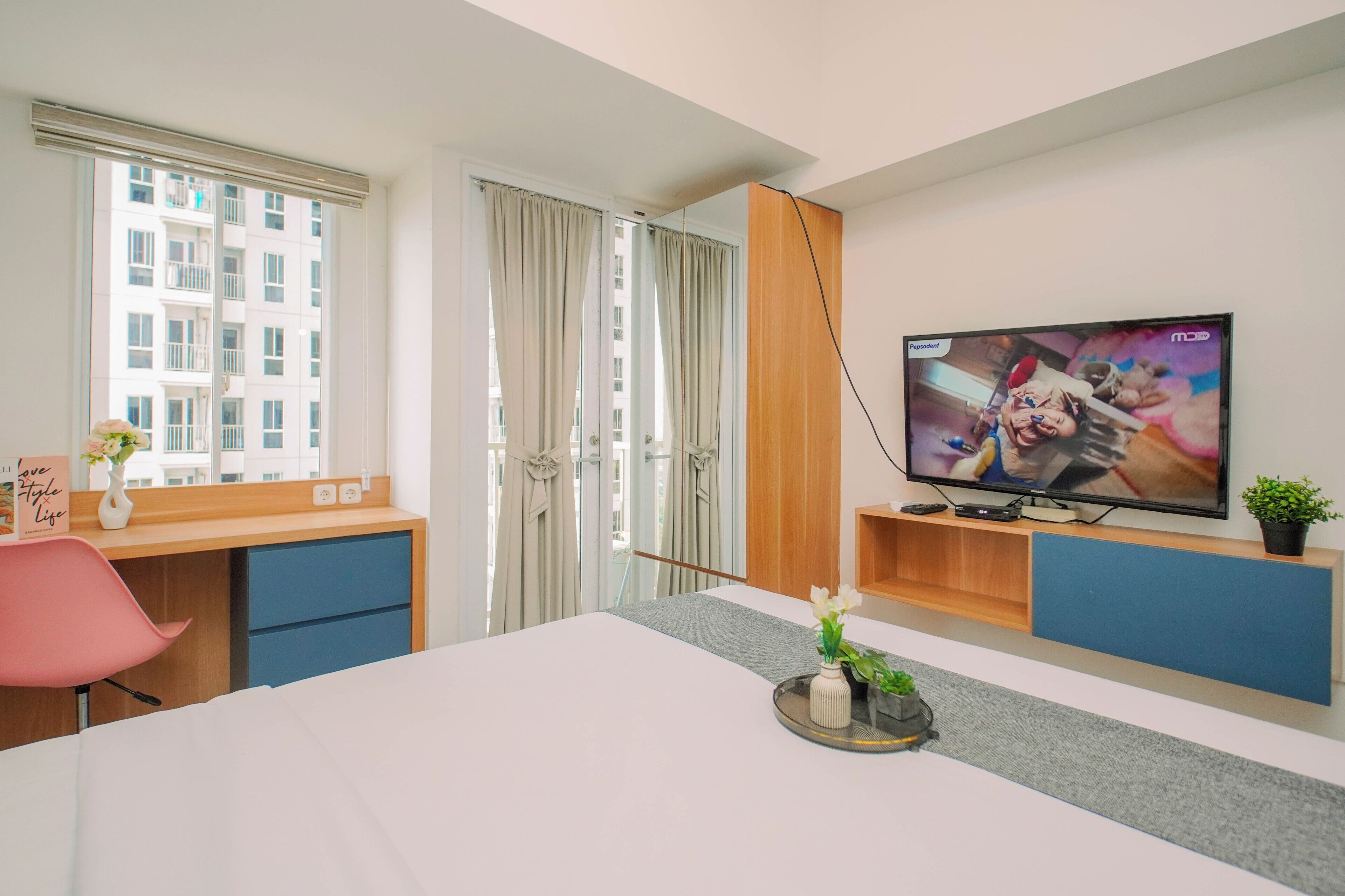 Hotellihuone, jossa on sänky, televisio, työpöytä ja ikkuna, jossa on verhot.