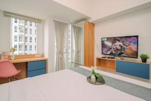 A hotel room with a bed, a TV, a desk, and a window with curtains.