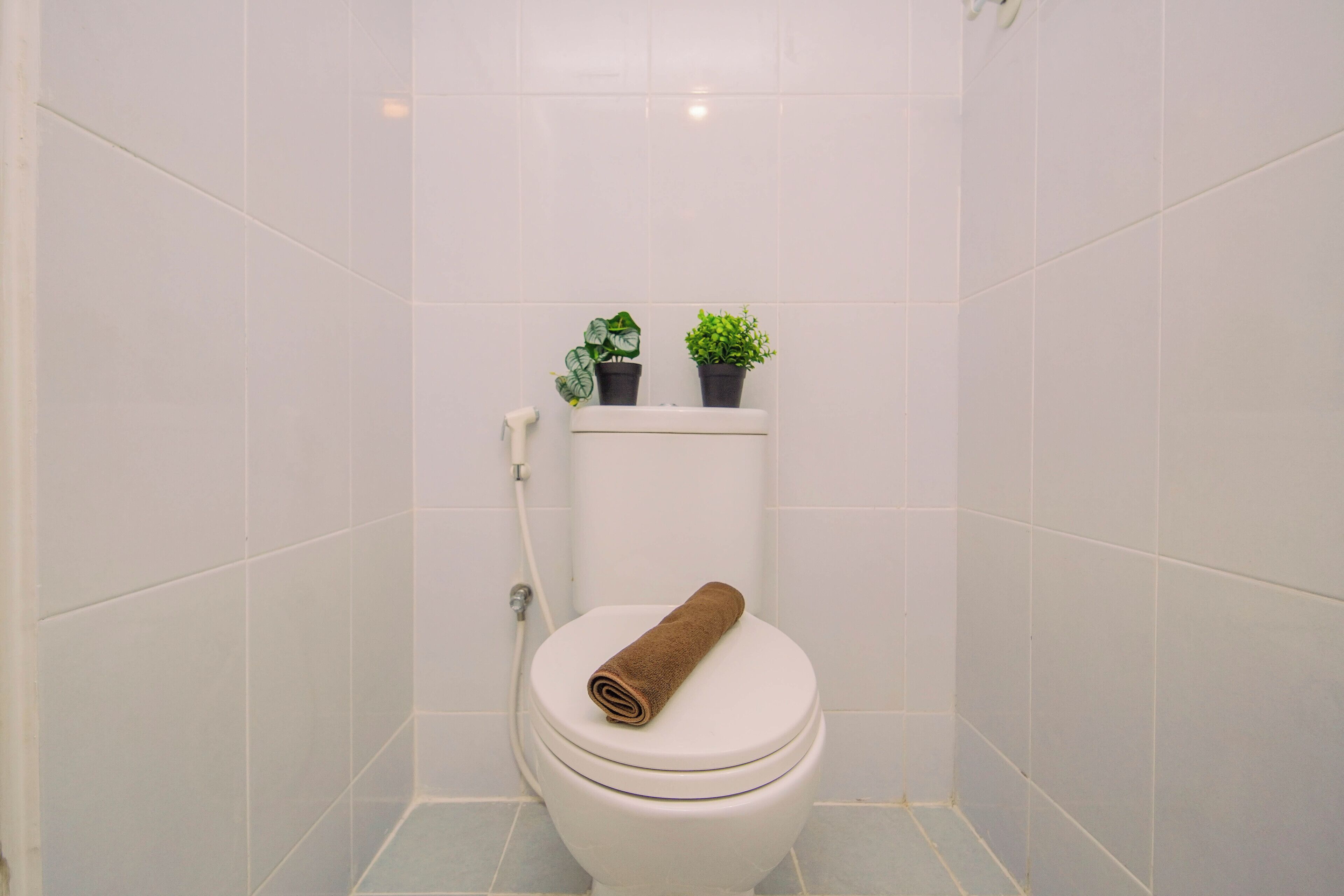 A bathroom with a white toilet, a towel on the seat, and two potted plants on the tank.
