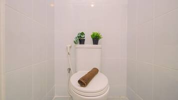 A bathroom with a white toilet, a towel on the seat, and two potted plants on the tank.